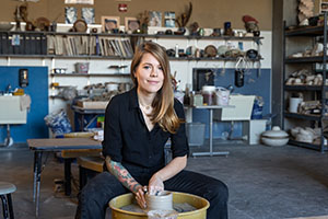 EvCC Ceramics student Jessica Mudd poses at pottery wheel in ceramics studio