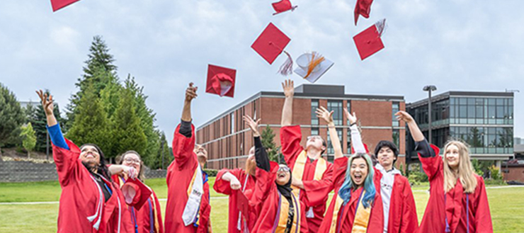 A group of EvCC Graduates in gowns, celebrate their achievements by tossing their caps in the air!