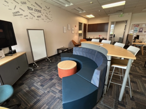 Tech Lounge open area with sofa seating, table seating for four, TV, and whiteboard