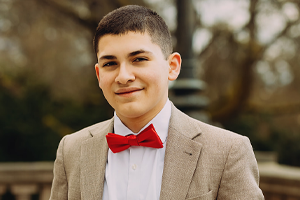 A picture Aristotle Ronyak in front of several trees, wearing a red bowtie. 