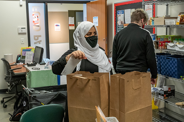 Two people work inside a room filled with stocked food shelves and grocery bags.