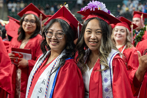 Chloe and a friend pose at commencement in their grad cap and gown.