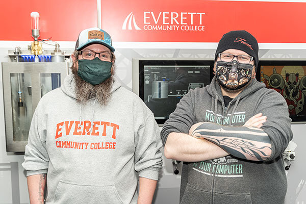 EvCC student Chris Von Reybyton (right) with fellow student pose in front of EvCC's cybersecurity wall.