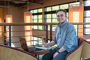 EvCC student Johann Macadangdang smiling at camera while working on laptop computer.