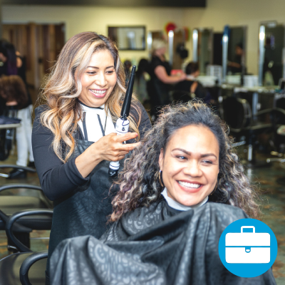 A student styles a client's hair, with an icon of a briefcase in the corner.