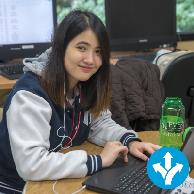 A student works on a laptop, with an icon of an arrow pointing three directions in the corner.