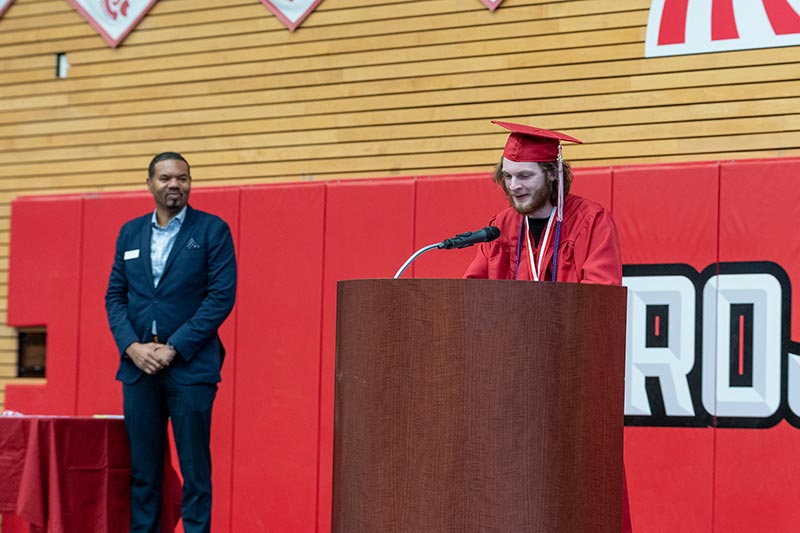 Steven Dion speaks at podium during EvCC's 2022 Outstanding Graduates ceremony with Dr. Darrell Cain looking on.