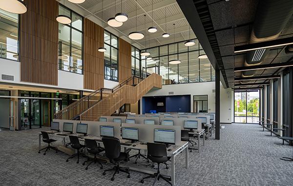 a light filled airy space with a large, open staircase leading to the upper floor and rows of computer stations in the foreground