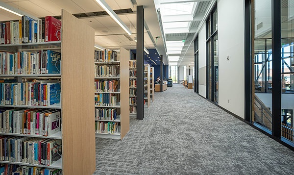 stacks of books on the left side, a hallway in the middle, and windows showcasing the atrium to the lower floor on the right