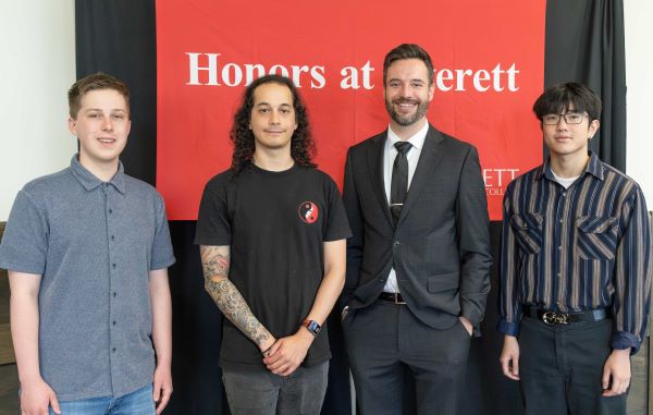 Four people stand in front of a red sign that says Honors at Everett.