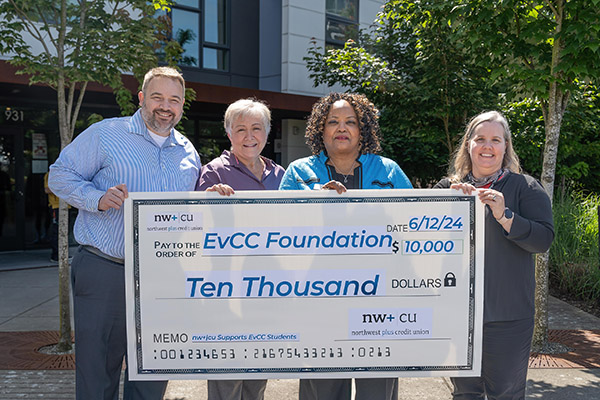 Four people stand outside holding a giant check that indicates NW+CU is donating $10,000 to the EvCC Foundation.