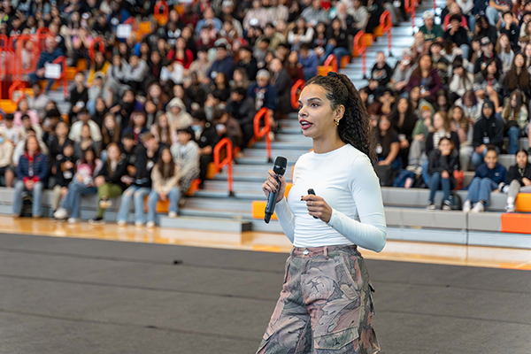 A speaker holds a microphone in front of a crowd filling the bleachers.