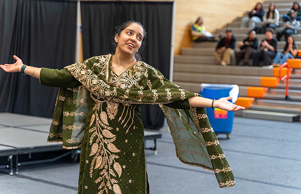 A dancer in traditional dress dances in a gymnasium.