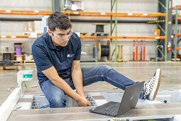 A man working in a manufacturing plant with tools and a laptop.