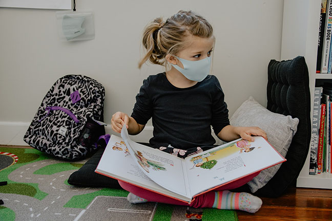 Child with a face mask reading a book.