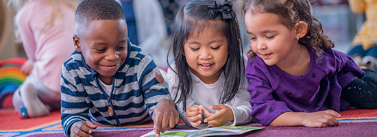 Three preschool children reading a book together.