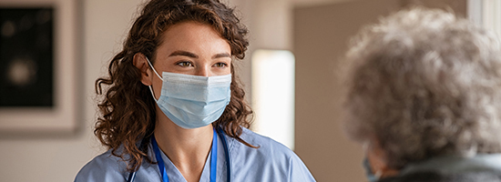 Female healthcare professional with a mask speaks with an old woman. 