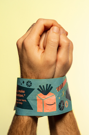 Logan Maruszak- photo of a persons hands bound with Amazon-brand packing tape on a yellow ground.