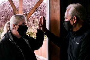 bob reese- staged photo of two people with masks with their palms pressed against glass.
