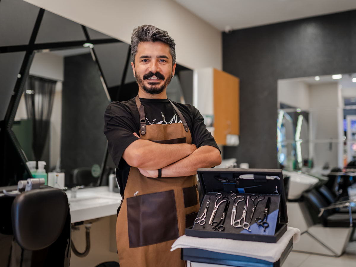 Student in an apron stands with arms crossed next to box of scissors for hair styling