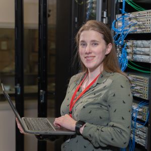 Student holds a laptop in front of a server wall