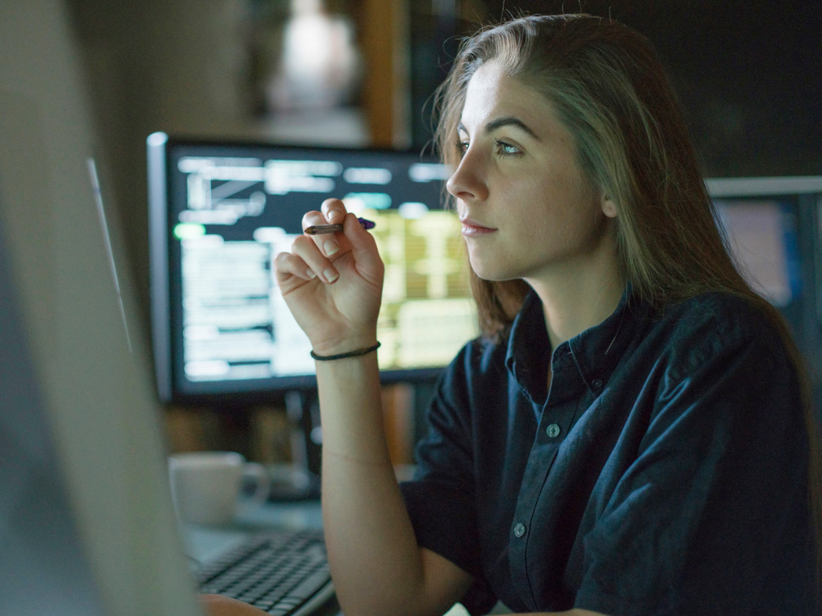 Student in front of computer monitors holding pen