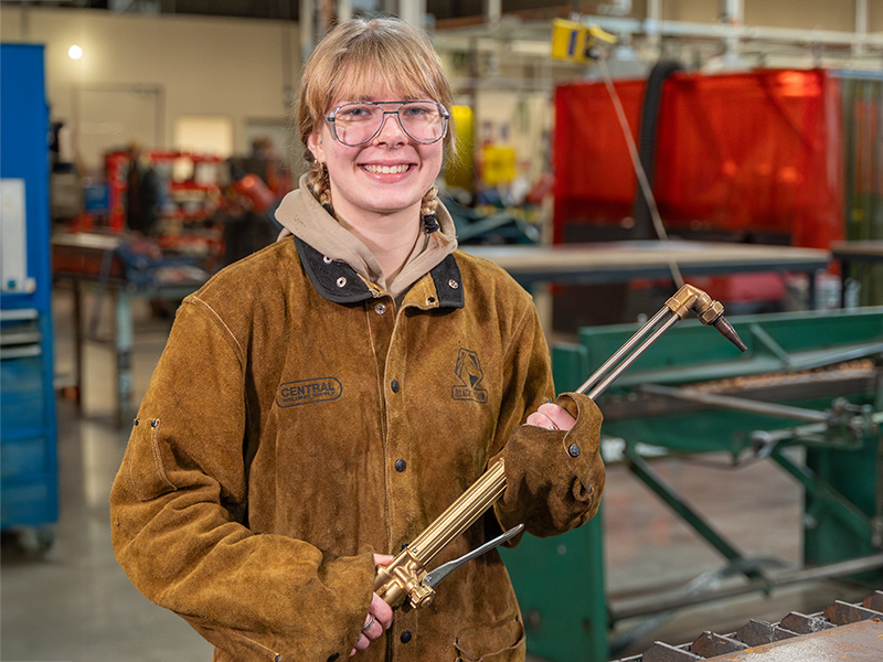 Student in welding jacket holds welding tool