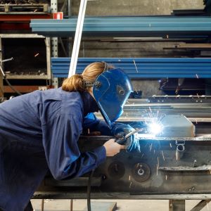 Student with welding mask and uniform actively performing a weld