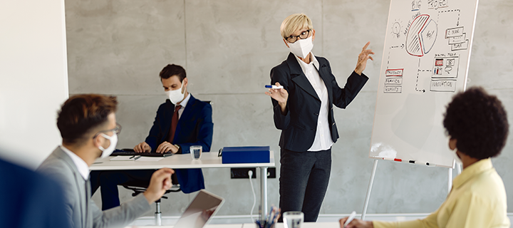 woman teaching a class of professionals while wearing a mask